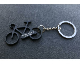 May include: Black metal bicycle keychain with a bottle opener. The keychain has the text "Gute Fahrt" and "Deine Marie" engraved on it.