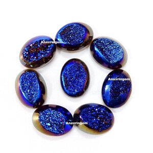 Puede incluir: Un conjunto de siete gemas ovaladas pulidas. Cada piedra tiene un borde exterior oscuro e iridiscente y un centro azul profundo y brillante. Las gemas están dispuestas en un círculo sobre un fondo blanco.