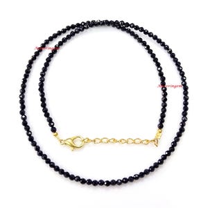 May include: A black beaded necklace with a gold clasp. The necklace is made of small, round beads and is approximately 18 inches long.