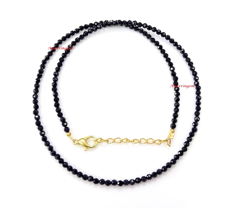May include: A black beaded necklace with a gold clasp. The necklace is made of small, round beads and is approximately 18 inches long.