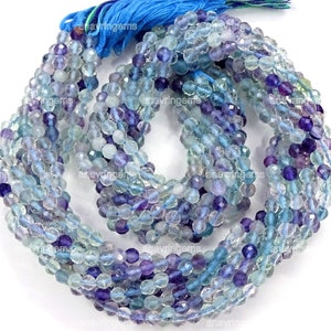 May include: A strand of blue and purple faceted fluorite beads. The beads are approximately 4mm in size and are strung on a clear elastic cord.