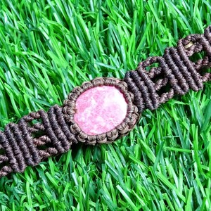 May include: A brown macrame bracelet with a pink and white gemstone in the center.