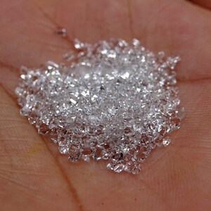 Puede incluir: Un montón de pequeños cristales transparentes y facetados, que se asemejan a diamantes, en la mano de una persona.