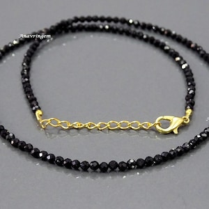 May include: A black gemstone necklace with a gold clasp. The necklace is made of small, round beads.