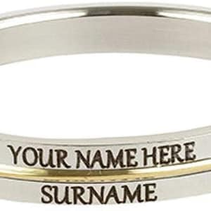May include: A silver-colored band with a gold-colored stripe in the middle. The text "YOUR NAME HERE" and "SURNAME" are engraved on the band. The band is likely made of stainless steel.
