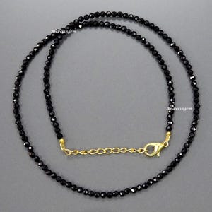 Puede incluir: Un collar de cuentas negras con un extensor de cadena dorada. El collar está hecho de cuentas pequeñas y redondas y tiene un diseño simple y elegante.