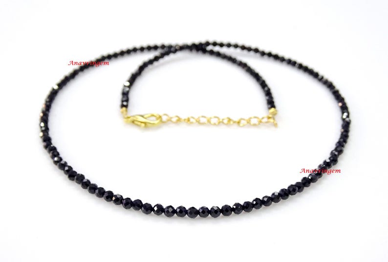 May include: A delicate black spinel gemstone necklace with a gold clasp. The necklace is made of small, round beads and is approximately 18 inches long.