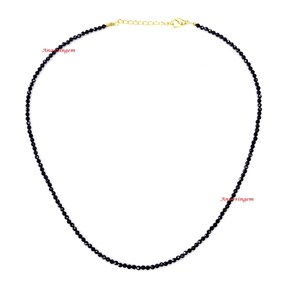 May include: A black beaded necklace with a gold chain clasp. The necklace is made of small, round beads and is approximately 18 inches long.