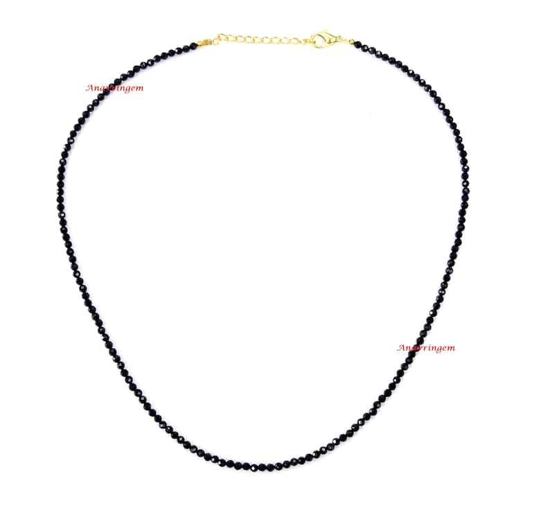 May include: A black beaded necklace with a gold chain clasp. The necklace is made of small, round beads and is approximately 18 inches long.
