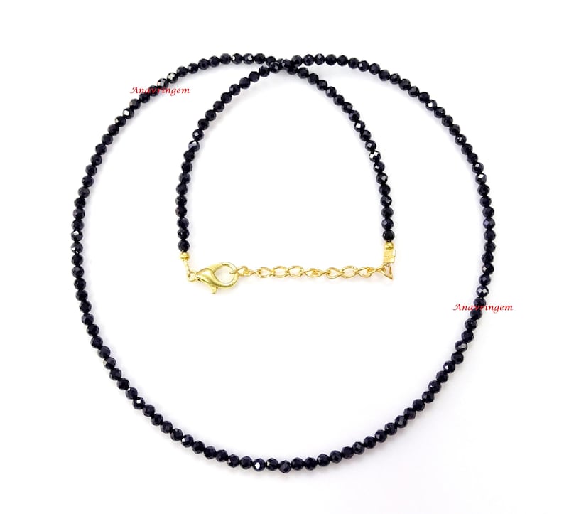 May include: A black gemstone necklace with a gold clasp. The necklace is made of small, round beads and is approximately 18 inches long.