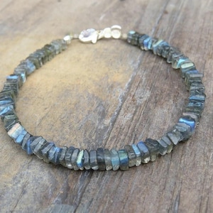 May include: A silver chain bracelet with dark blue labradorite gemstone beads. The beads are faceted and have a shimmery iridescent effect.