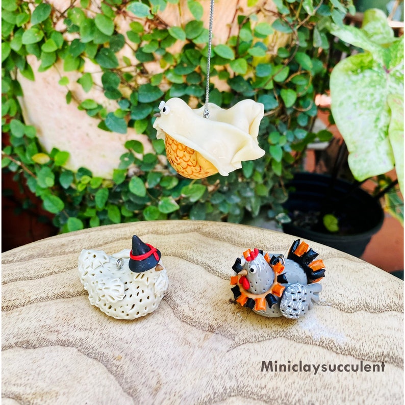 May include: Three handmade polymer clay ornaments in the shape of a ghost, a witch, and a turkey. The ghost is white with a yellow face and black eyes. The witch is white with a black hat and red accents. The turkey is gray with orange and black feathers.