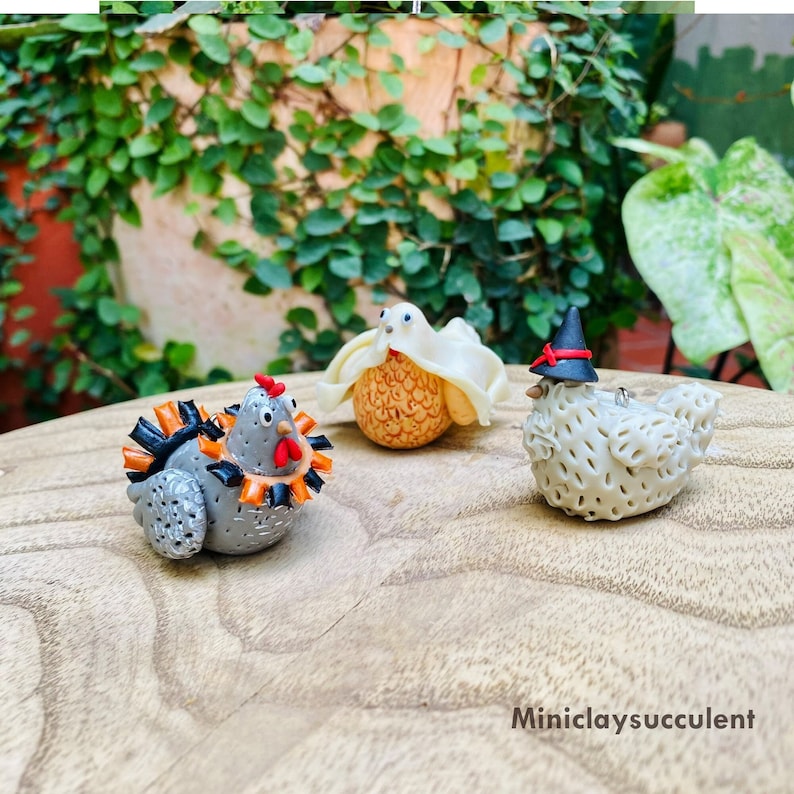 May include: Three small clay figurines of chickens dressed up for Halloween. One chicken is a ghost, one is a witch, and one is a turkey.