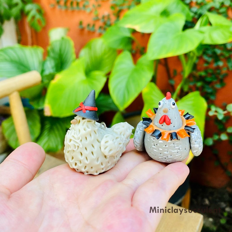 May include: Two handmade ceramic chicken figurines. One is white with a black witch hat and the other is gray with an orange and black collar.