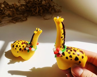 May include: Two yellow and brown giraffe figurines with black spots and red and white flower garlands around their necks.