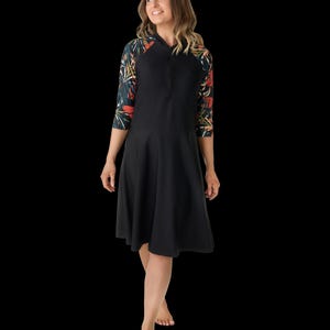 May include: A black dress with three-quarter sleeves featuring a floral pattern in red, orange, and green. The dress has a hood and a zipper down the front. The skirt flares out from the waist.