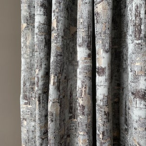 May include: Close-up of a set of curtains with a textured, abstract pattern in shades of gray, brown, and gold.