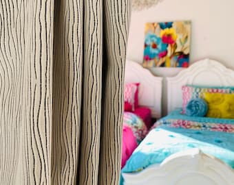 May include: A white bed with a blue and pink patterned comforter and pillows. The bed is in a bedroom with a beige curtain with black stripes.