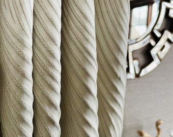 May include: Close-up of beige fabric curtains with a subtle diagonal stripe pattern. The fabric has a textured, woven look.