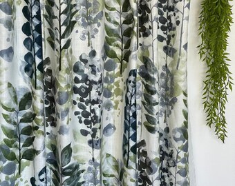 May include: A white fabric with a green, blue, and black watercolor floral pattern. The fabric has a linen texture.