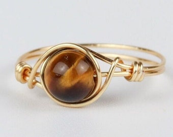 May include: Gold wire wrapped ring with a round tiger's eye gemstone.