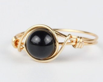 May include: A gold wire ring with a black gemstone. The ring is wrapped in gold wire and has a simple design.