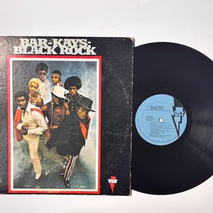 May include: A vintage vinyl record album by Bar-Kays, titled "Black Rock." The album cover shows a group of men in colourful outfits. The record is black with a blue label.