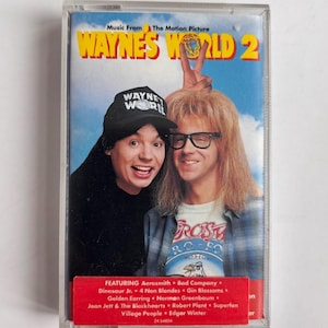 Könnte beinhalten: Eine Musikkassette für den Film "Wayne's World 2" mit dem Filmtitel und Bildern der beiden Hauptfiguren. Das Cover enthält eine Liste der Künstler wie Aerosmith und Joan Jett.