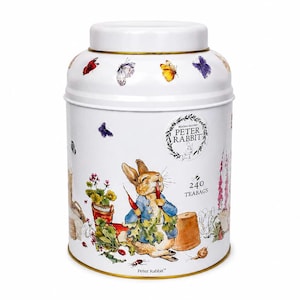 May include: A white cylindrical metal tea tin featuring a Peter Rabbit illustration, colourful butterflies, and garden elements. The text reads Beatrix Potter Peter Rabbit and 240 teabags. The container has a matching white lid with a gold-toned rim.