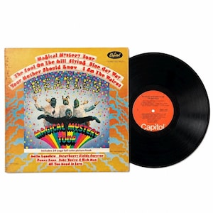 May include: The Beatles Magical Mystery Tour vinyl record and album cover. The yellow cover features the band in animal costumes, a rainbow graphic, and song titles including The Fool On The Hill and I Am The Walrus. The black vinyl has an orange label.