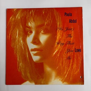 Könnte beinhalten: Albumcover mit Paula Abdul, orangefarbenem Haar und rotem Hintergrund. Der Text auf dem Cover lautet "Paula Abdul" und "(It's Just) The Way That You Love Me."