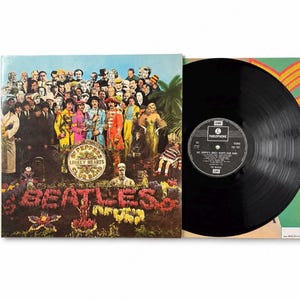 May include: A vinyl record album cover with a vibrant group of people and the text "Sgt. Pepper's Lonely Hearts Club Band" and the band name "BEATLES" in floral letters. A black vinyl record is next to the cover.
