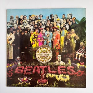 May include: Album cover featuring a crowd of people and The Beatles in colorful military-style outfits. The album title "Sgt. Pepper's Lonely Hearts Club Band" is on a drum. The word "BEATLES" is spelled out in flowers.