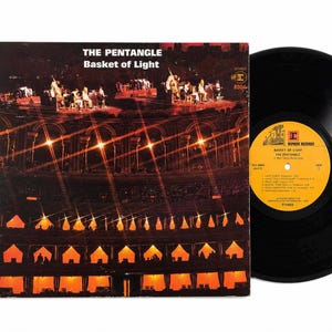 May include: A vinyl record and its square cardboard cover titled Basket of Light by The Pentangle. The cover features a dark, multi-tiered architectural structure illuminated by bright orange lights. The record has a yellow center label with black text.