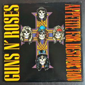 May include: Black album cover with the Guns N' Roses logo in yellow and the words "Appetite for Destruction" in red. The cover art shows a cross with skulls wearing hats and sunglasses.