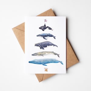 May include: A white card with watercolour illustrations of five whale species, arranged vertically. The whales are in shades of blue, grey, and black. A brown envelope is behind the card.