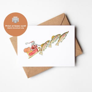 May include: A whimsical Christmas card featuring Santa Claus in a red suit and sleigh, pulled by four colorful fish. The card has the text "Print at home card! digital download only" in a brown circle.