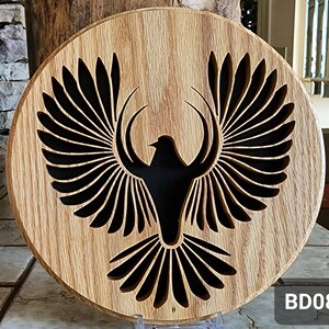 May include: A wooden wall decor with a black silhouette of a bird with its wings spread out. The bird is carved into the wood and the background is a natural wood grain.