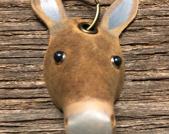 May include: A brown leather donkey keychain with gray ears and black eyes. The keychain has a brass ring attached to the top.