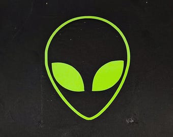 May include: A neon green alien head graphic with large almond-shaped eyes. The alien head is outlined in green and set against a black background. The image also includes other green geometric shapes.