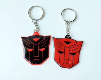 May include: Two keychains featuring the Transformers Autobot logo. One keychain is red and the other is black.