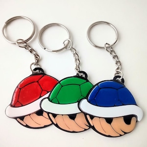 May include: Three keychains featuring a cartoon character from a popular video game. Each keychain has a different colored shell: red, green, and blue. The shells have white accents and a cartoon face.