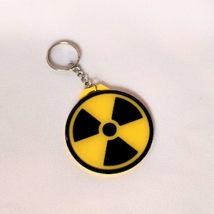 May include: A yellow keychain with a black radiation symbol. The keychain is attached to a silver ring.