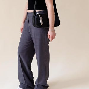 May include: A person wearing a black crop top and grey wide-leg trousers with a black shoulder bag.