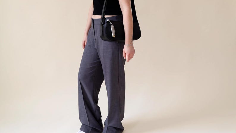 May include: A person wearing a black crop top and grey wide-leg trousers with a black shoulder bag.