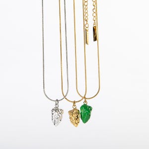 Op de afbeelding: Drie gouden kettingen met verschillende hangers. De hangers zijn in de vorm van een zilveren, gouden en groene nugget.