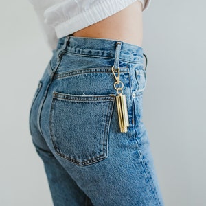 May include: A person wearing blue denim jeans with a gold keychain attached to the back pocket.