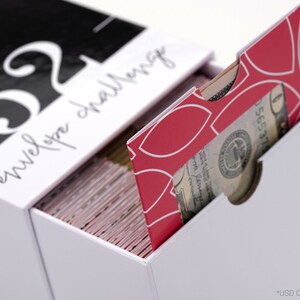 以下が含まれることがあります： 前面に「52 envelope challenge」という文字が印刷された白い箱。箱が開いており、白地に幾何学模様が描かれた赤い封筒が引き出されている。封筒には窓があり、米ドル紙幣が見えている。