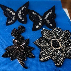 May include: Four decorative patches featuring two black butterfly shapes embellished with silver sequins, one black floral motif with dark beads and sequins, and one star-shaped patch covered in dense black and silver sequins and beads.