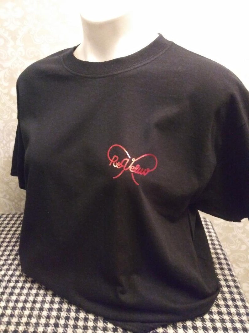 May include: A black short-sleeved t-shirt featuring a red metallic graphic on the chest. The graphic consists of a stylized infinity symbol shape with the text "ReVeluv" written in a cursive script font integrated into the center of the design.